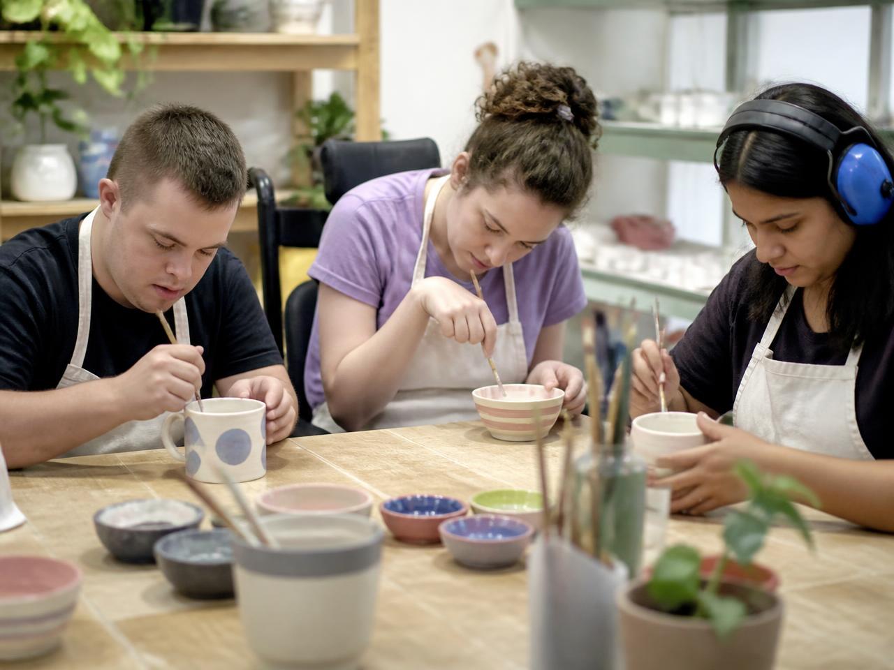 A young adult shaping clay at a pottery wheel in a bright studio